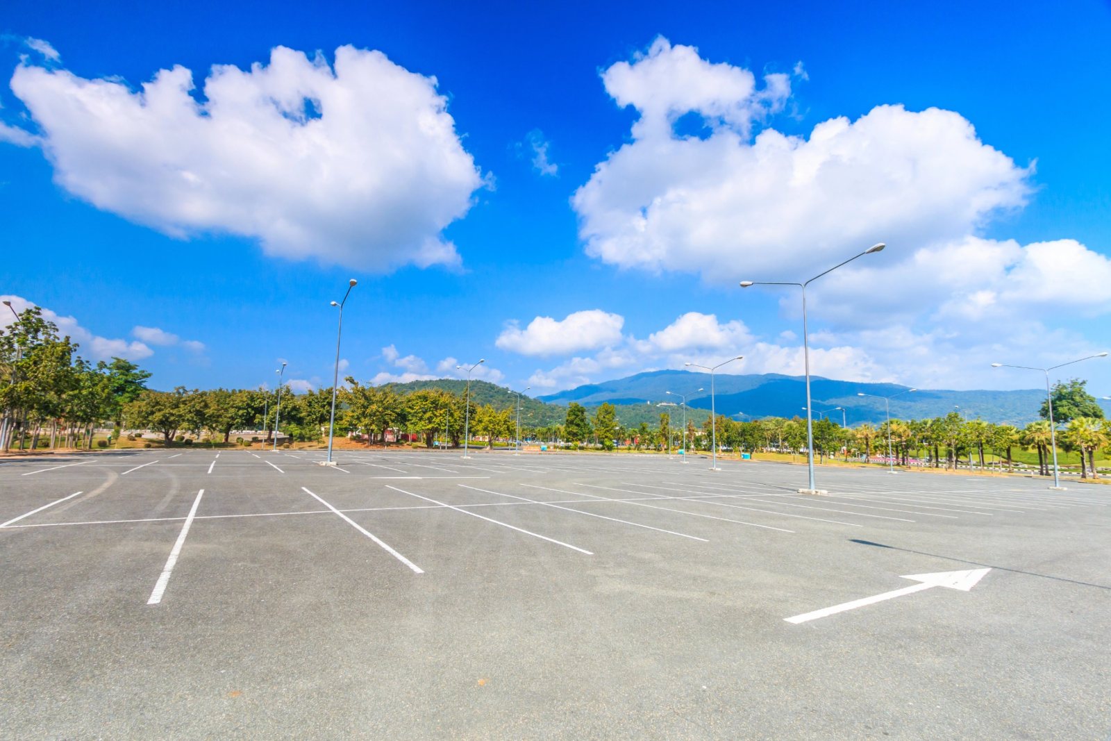 Wide, empty asphalt parking lot under full sun with no shade