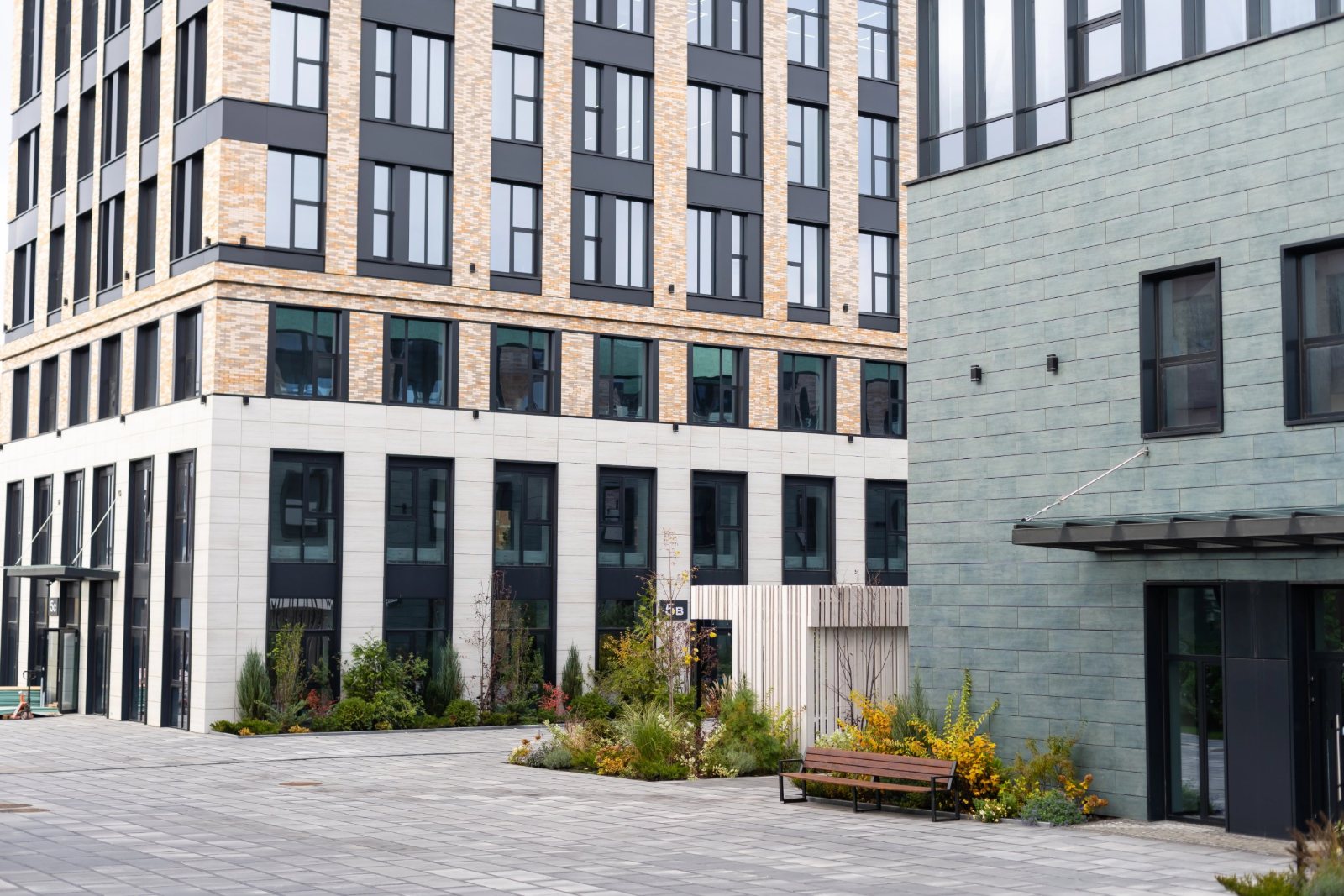 Mid-rise mixed-use buildings with ground-floor glazing around a paved, planted plaza